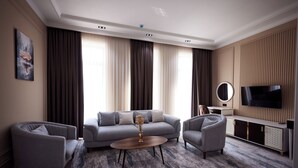 A modern living room with a grey sofa, two armchairs, a coffee table, and a TV on a wooden cabinet. - Noble Samarkand (Samarkand)
