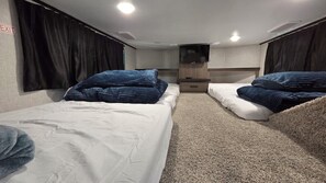 Dormitori d'una caravana domèstica, amb dos llits, una televisió i un petit moble d'emmagatzematge.