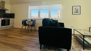 A modern living room with a black sofa, a glass coffee table, and a dining area with a table and chairs. - Viewforth Studio No.3 (Fort William)