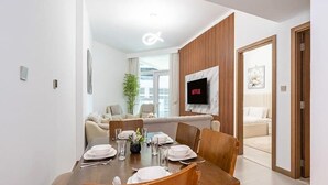 Un comedor moderno con una mesa de madera dispuesta para cuatro personas, un televisor montado en la pared y un sofá al fondo.