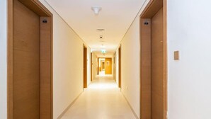 Un long couloir étroit, typique d’un hôtel, avec des portes en bois de chaque côté et un plancher de couleur claire.