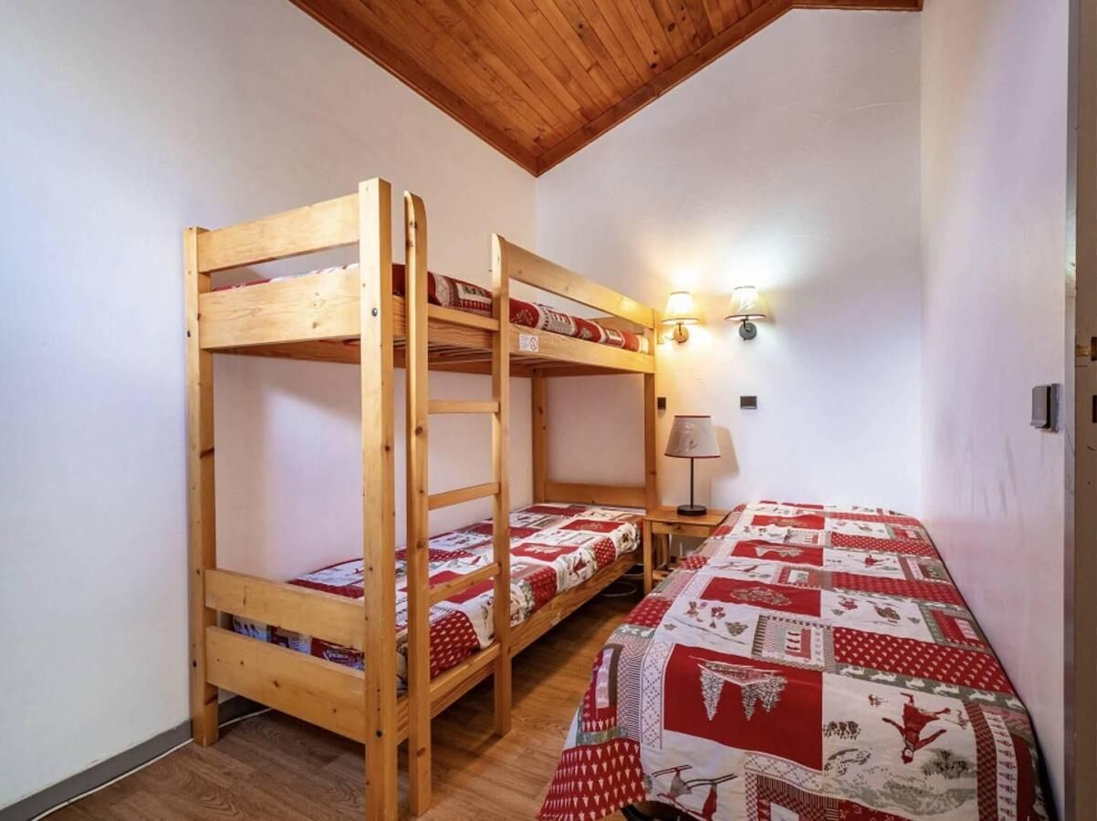 Una habitación con dos literas y una cama individual, paredes de madera, techo inclinado y una lámpara fijada a la pared.