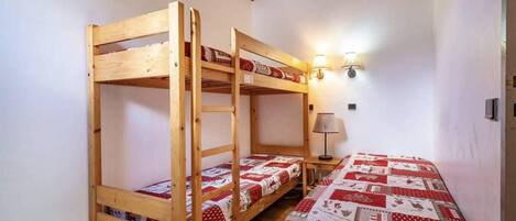 Una habitación con dos literas y una cama individual, paredes de madera, techo inclinado y una lámpara fijada a la pared.