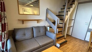 A modern living room with a grey sofa, a wooden coffee table, a staircase with wooden steps, and a framed picture on the wall. - 40m from ski slopes, 5th floor, view valley, balcony, tv, 50m², Méribel-Mottaret (Méribel - Les Allues)