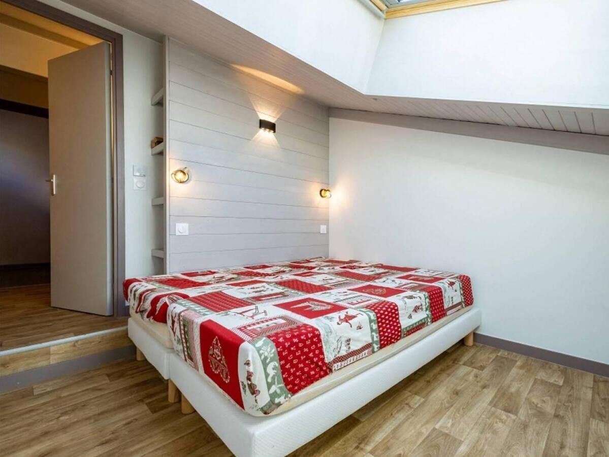 Una camera da letto con un letto, pavimento in legno, una parete bianca e un velux.