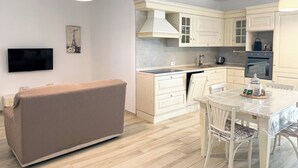 A modern kitchen with white cabinets, a built-in oven, and a dining area with a table and chairs.