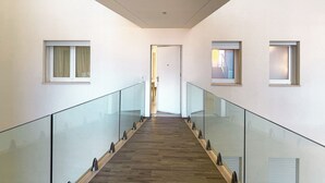 A modern interior with a glass railing, wooden flooring, and a door at the end of a hallway.