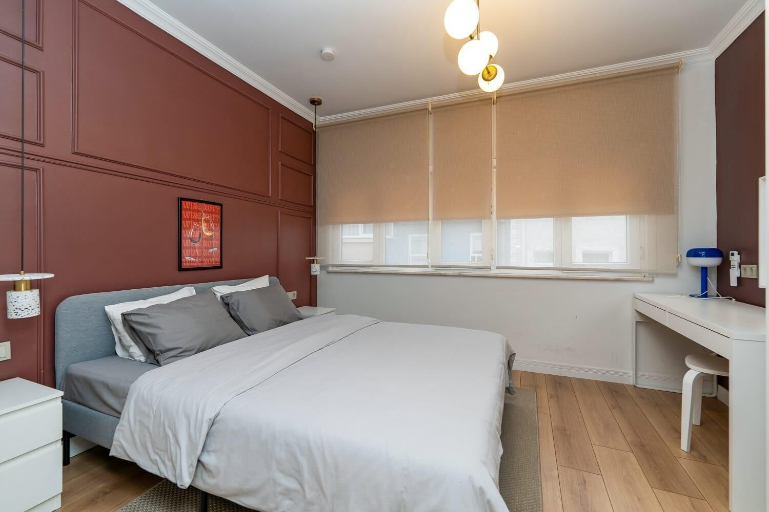 A bedroom with a bed, bedside tables, a desk, and a window with blinds.