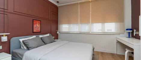 A bedroom with a bed, bedside tables, a desk, and a window with blinds.