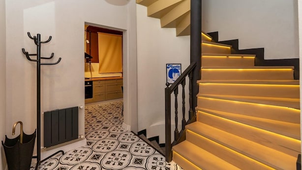 Una escalera con escalones iluminados, un perchero, un radiador y un suelo con diseño.