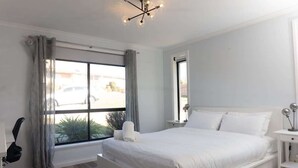 A bedroom with a large bed, a desk, a chair, a window with curtains, and a ceiling light fixture. - Beautiful Mountain Views (Prospect Vale)