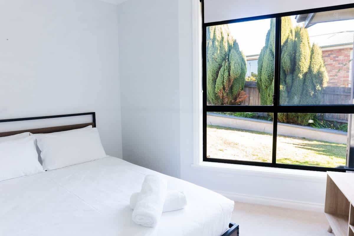 Una habitación de hotel con una cama, un ventanal con vistas a árboles y una banca de madera.
