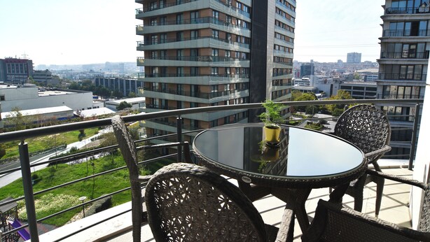 A balcony with wicker furniture, a glass table, and a potted plant.