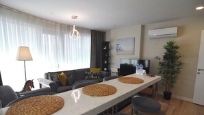 A modern living room with a long white table, grey sofas, and a TV.