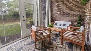 A patio with a brick wall, a wooden table, two chairs, and a sofa. - Oh Gosh! So Posh in Myrtlewood Villas (Myrtle Beach)