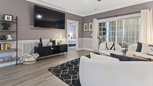 A modern living room with a flat-screen TV, a ceiling fan, a large window with curtains, and a black and white sofa set. - Oh Gosh! So Posh in Myrtlewood Villas (Myrtle Beach)