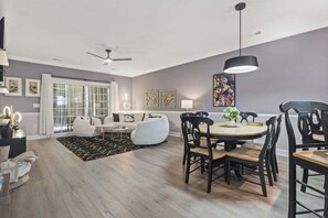Uma sala de estar moderna com sofá, cadeiras, uma mesa de jantar e um ventilador de teto.