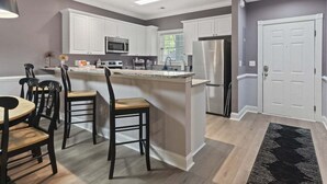 A modern kitchen with white cabinets, a central island, a dining area with chairs, and a refrigerator. - Oh Gosh! So Posh in Myrtlewood Villas (Myrtle Beach)