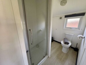 Un baño pequeño con cabina de ducha de vidrio, un inodoro y una ventana.