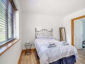 A bedroom with a bed, a bedside table, a mirror, and a window with blinds. - 3 bedroom accommodation in Lowestoft (Lowestoft)