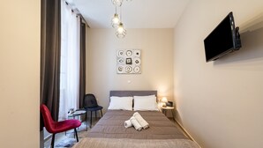 A hotel room with a bed, a TV, a chair, a table, and a wall art piece.