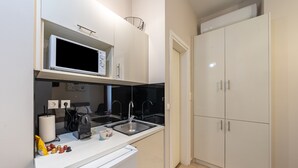 A modern kitchen with white cabinets, a microwave, a sink, and a coffee machine.