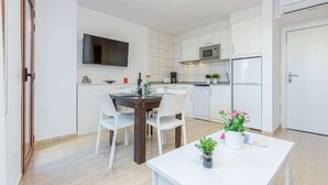 Et moderne køkken med hvide skabe, en mikroovn, et køleskab og et spisebord med stole.