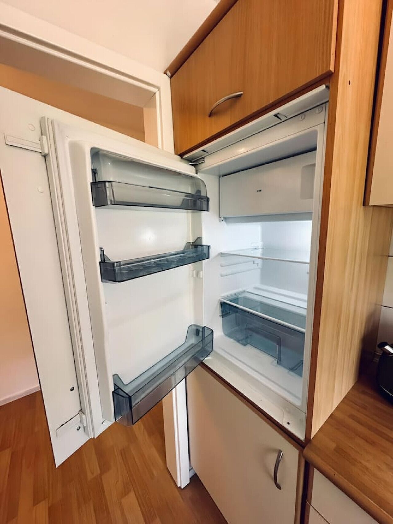 Eine kompakte Küche mit integriertem Kühlschrank, Holzschränken und einer kleinen Arbeitsplatte.