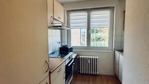 A compact kitchen with wooden cabinets, a built-in oven, and a window with blinds. - Apartment Euregio III - Central & close to the clinic (Nordhorn)