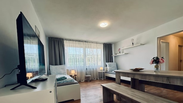A modern living room with a bed, a desk, a bench, and a dining table. - Apartment Euregio III - Central & close to the clinic (Nordhorn)