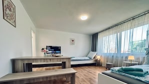A modern bedroom with a wooden floor, a bed with a blue blanket, a desk with a computer, and a window with curtains. - Apartment Euregio III - Central & close to the clinic (Nordhorn)
