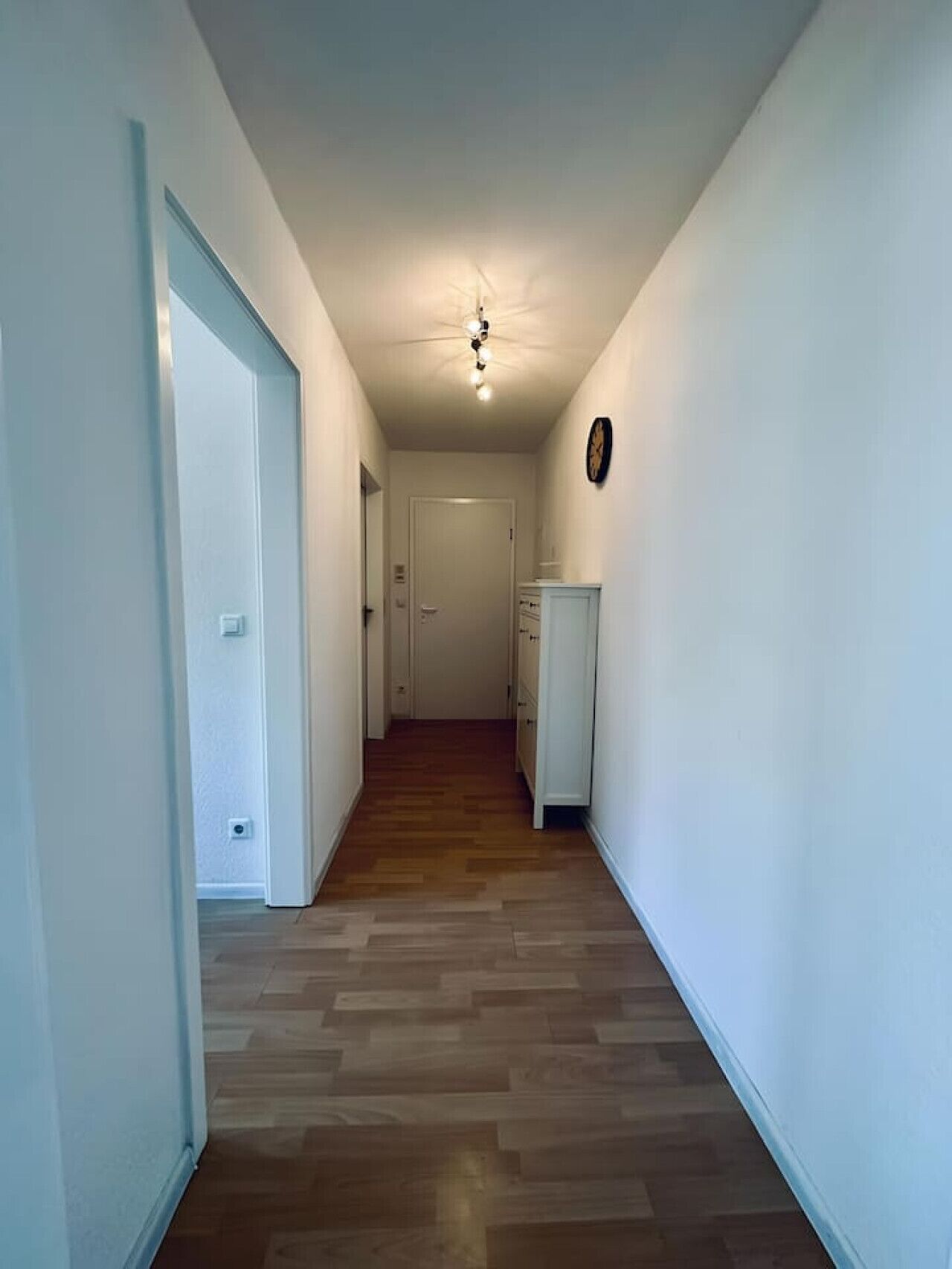 Ein Korridor mit Holzboden, weißen Wänden, einem Deckenventilator und einer Tür am Ende.