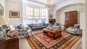 Een ruime woonkamer met een groot raam, een kroonluchter en een kamerbreed tapijt.