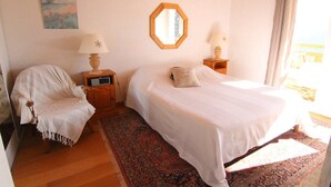 Een slaapkamer met een bed, een stoel, een nachtkastje, een spiegel en een schilderij aan de muur.