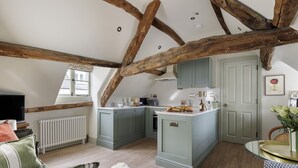 Ein gemütliches Loft-Zimmer mit freiliegenden Holzbalken, einer Küchenzeile, einer komfortablen Sitzecke und Blick auf die Stadt.