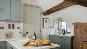 Eine Küche mit weißer Arbeitsplatte, einem Spülbecken und einer Decke aus Holzbalken. An der Wand befinden sich gerahmte Bilder und auf der Arbeitsplatte steht eine Kaffeemaschine.