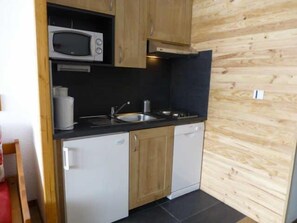 A compact kitchen with wooden cabinets, a microwave, a sink, and a dishwasher.