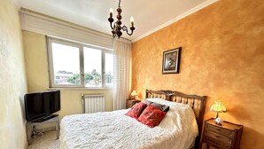 A hotel room with a large bed, a television on a stand, a radiator, and a window with a view of greenery. - 3-bedroom apartment in Fréjus with shared pool, near the center (Fréjus)