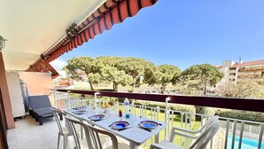 A balcony with a table set for two, white plastic chairs, and a view of a swimming pool and trees. - 3-bedroom apartment in Fréjus with shared pool, near the center (Fréjus)