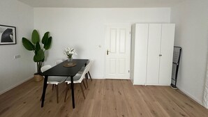 Une pièce comprenant une table à manger, des chaises, une plante en pot, une porte blanche et une armoire blanche.
