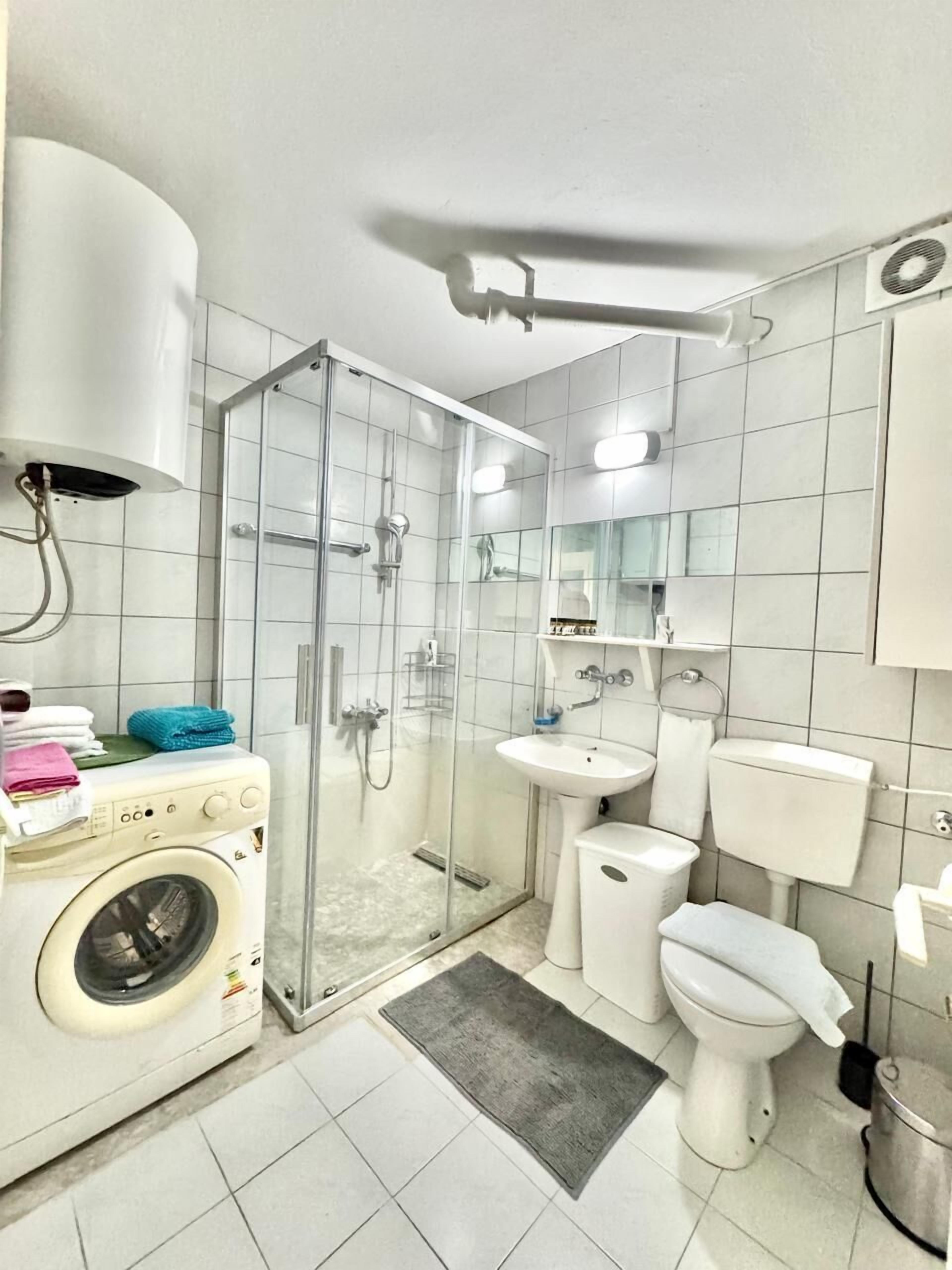 Ein modernes Badezimmer mit Duschkabine, Waschmaschine, Waschbecken, Toilette und Spiegel.