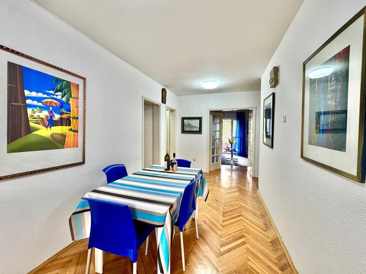A hotel room with a dining area featuring a table set for four, blue chairs, and a wooden floor.