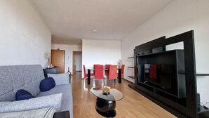 Una sala de estar moderna con un sofá gris, sillas rojas, una mesa de centro de vidrio y un televisor de pantalla plana grande montado en la pared.