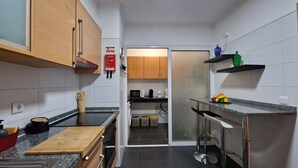 Cocina compacta con armarios de madera, microondas, cafetera y frutero sobre la encimera.