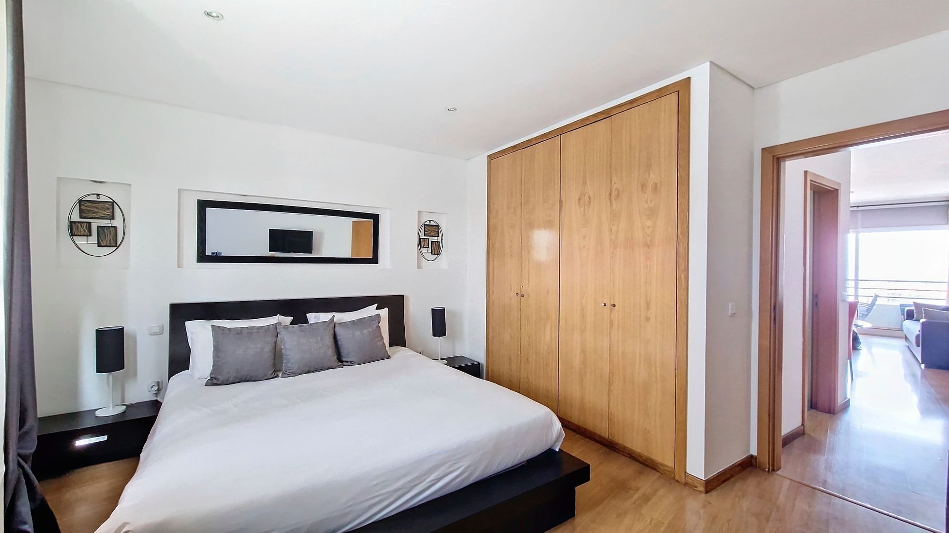 Quarto com cama, mesas de cabeceira, guarda-roupa e televisão na parede.