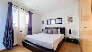Un dormitorio moderno con una cama grande, suelo de madera y una ventana con cortinas.