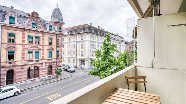 Een balkon met een houten bankje met uitzicht op een straat met historische gebouwen.