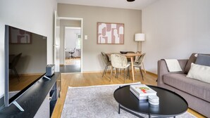 Een moderne woonkamer met een bank, een salontafel, een televisie, een eethoek met een tafel en stoelen, en een lamp.
