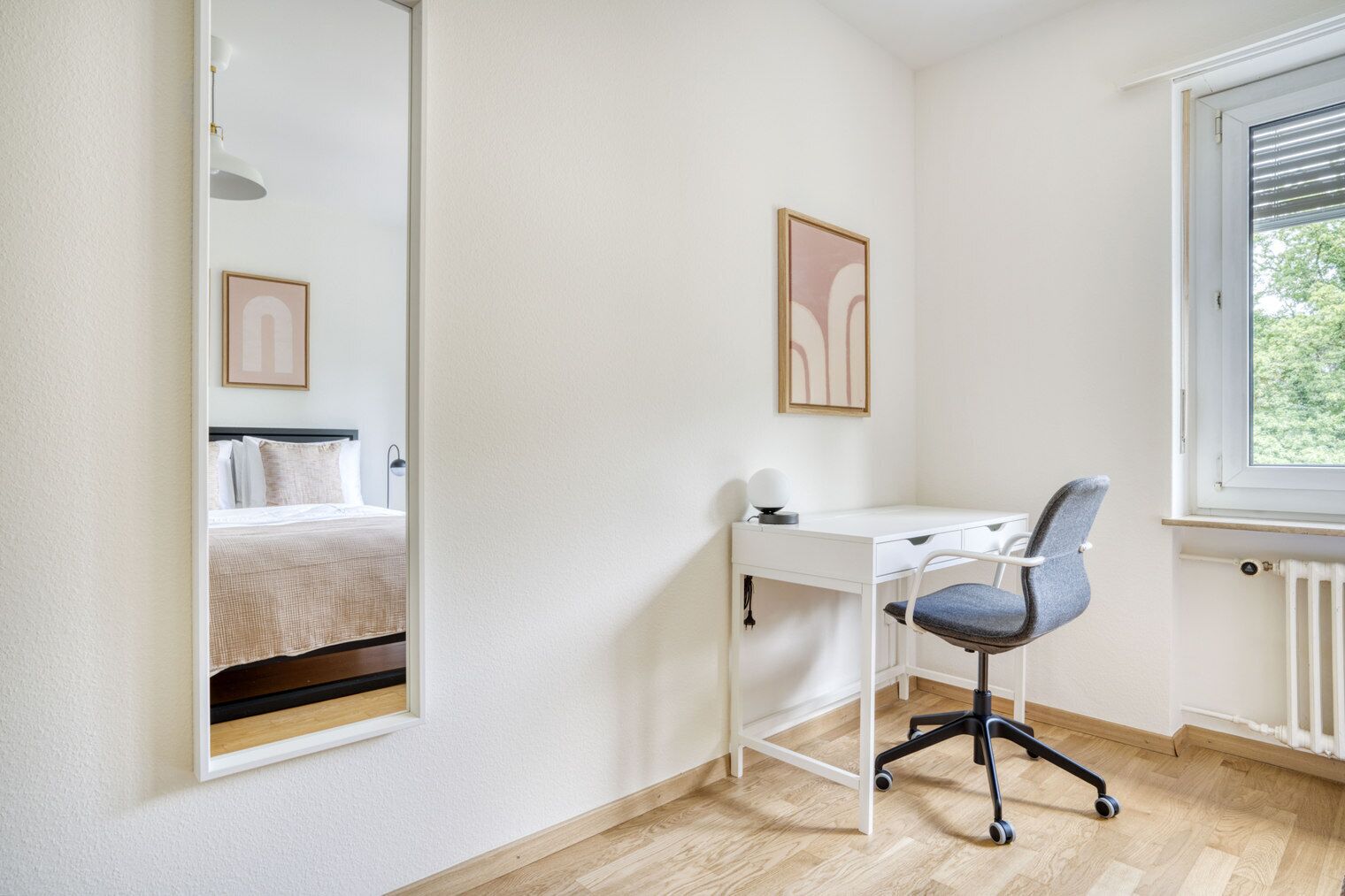 Une chambre à coucher avec un lit, un bureau et une chaise. Il y a une fenêtre qui donne sur les arbres.