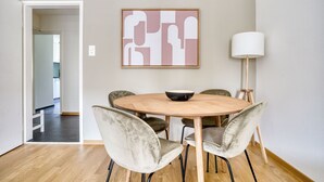 Een eetruimte met een ronde houten tafel, vier stoelen, een schaal, een abstract schilderij aan de muur en een vloerlamp.
